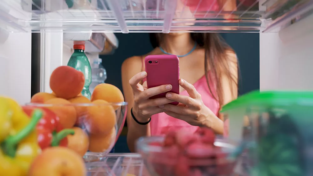 Žena ovl&aacute;d&aacute; nastaven&iacute; lednice přes mobiln&iacute; telefon_06