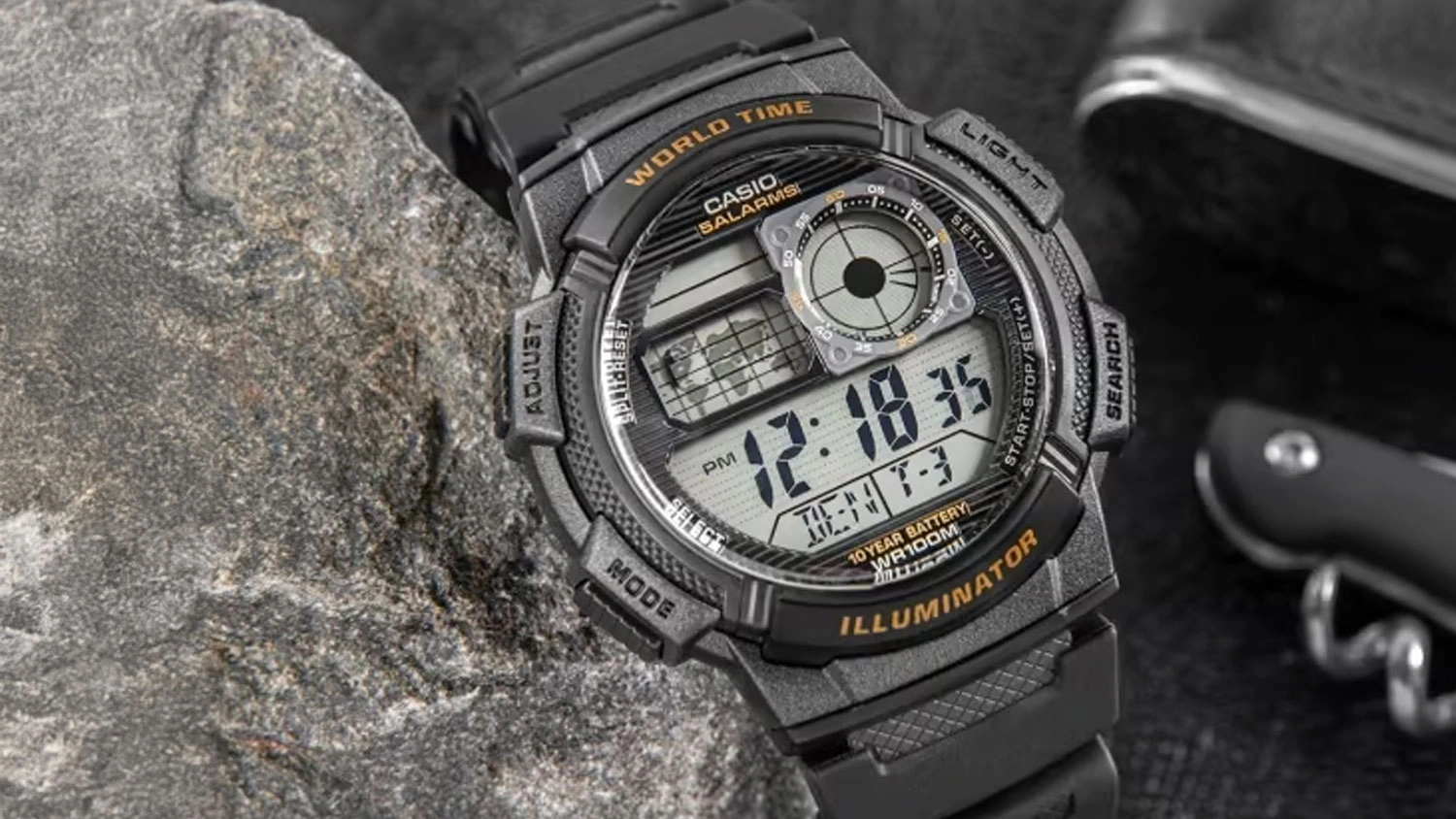 P&aacute;nsk&eacute; n&aacute;ramkov&eacute; hodinky Casio AE-1000W-5AVEF opřen&eacute; o k&aacute;men