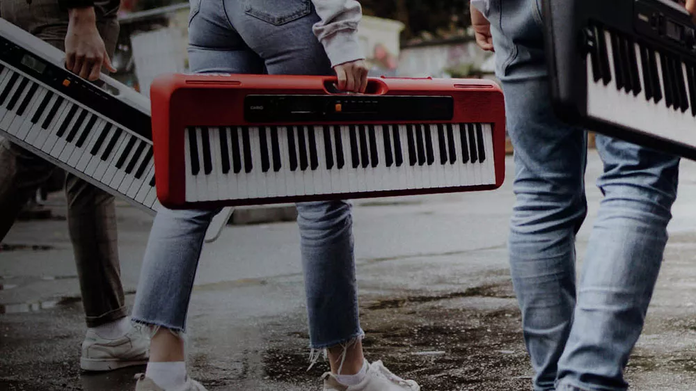 Pohled na 3 osoby nesoucí klávesy Casio CT-S300 za vestavěné madlo_02