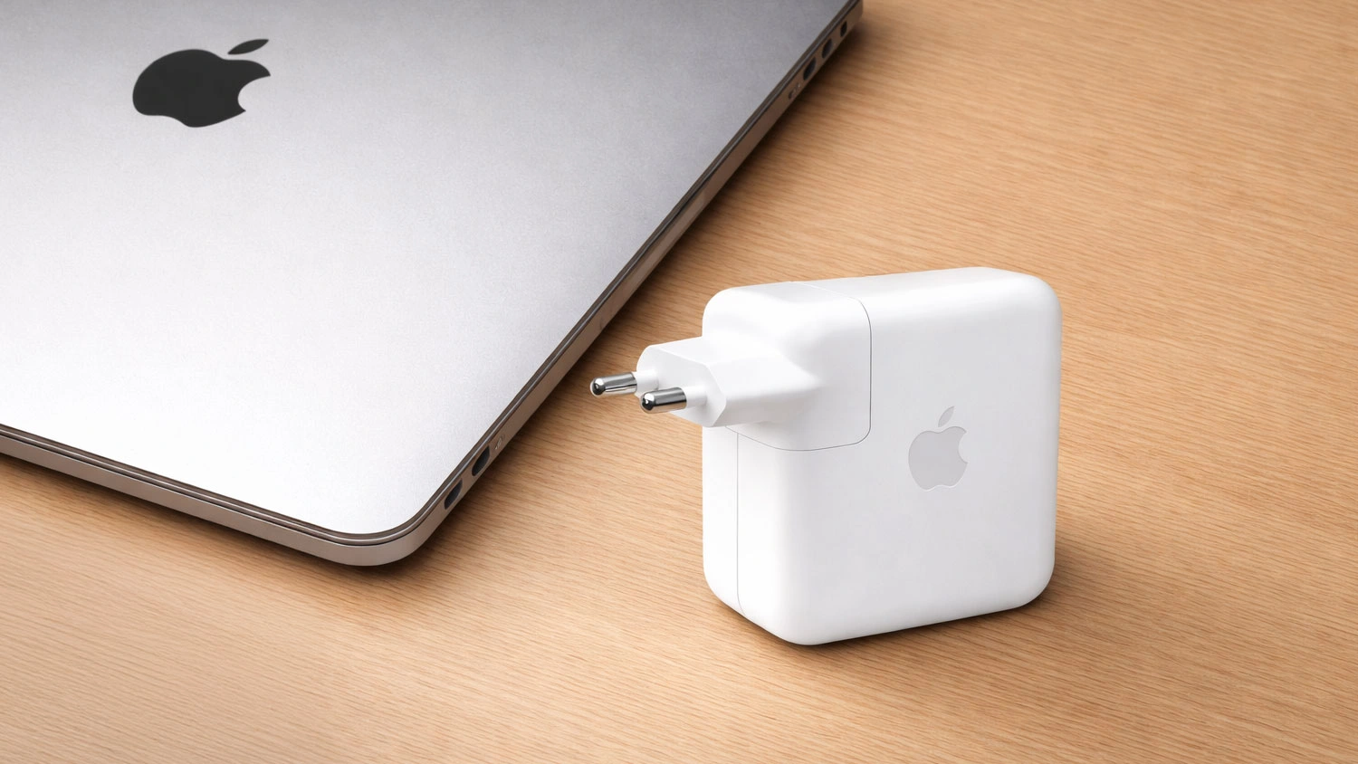 Napájecí adaptér Apple 70 W USB-C vedle notebooku na stole