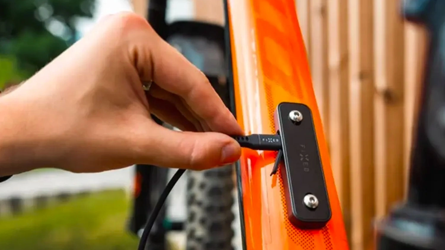 Ruka zapojuje nabíjecí kabel USB-C do Bluetooth lokátoru FIXED Tag Bikee připevněného k oranžovému rámu jízdního kola.