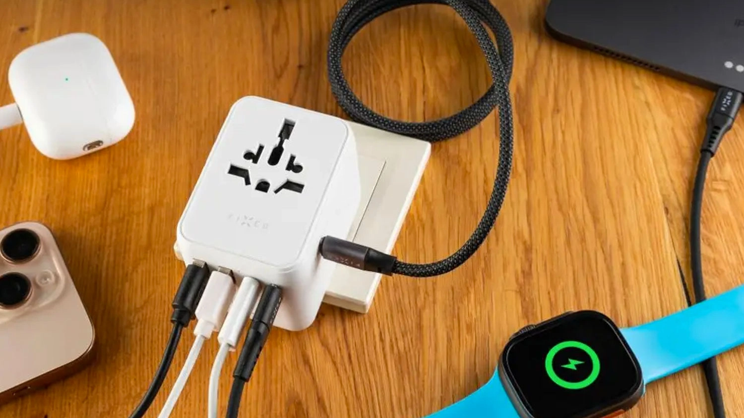 B&iacute;l&yacute; cestovn&iacute; adapt&eacute;r FIXED Voyager v z&aacute;suvce s několika připojen&yacute;mi kabely pro nab&iacute;jen&iacute; chytr&yacute;ch hodinek, sluch&aacute;tek a telefonů.