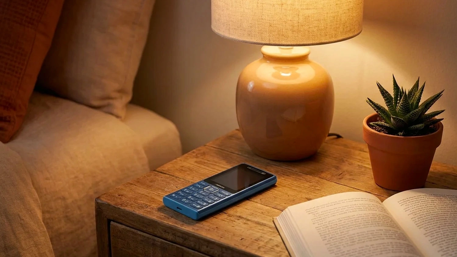 Mobilní telefon Nokia 210 4G položený na dřevěném stole vedle knihy.
