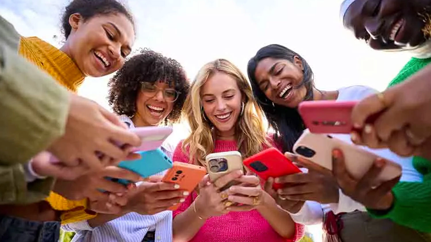 Skupina mlad&yacute;ch lid&iacute; se usm&iacute;v&aacute; a společně se d&iacute;v&aacute; do sv&yacute;ch mobiln&iacute;ch telefonů.