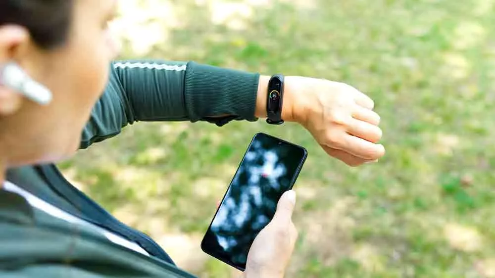 Žena ve sportovn&iacute;m oblečen&iacute; sleduj&iacute;c&iacute; fitness n&aacute;ramek na sv&eacute;m z&aacute;pěst&iacute; s mobiln&iacute;m telefonem v ruce_04