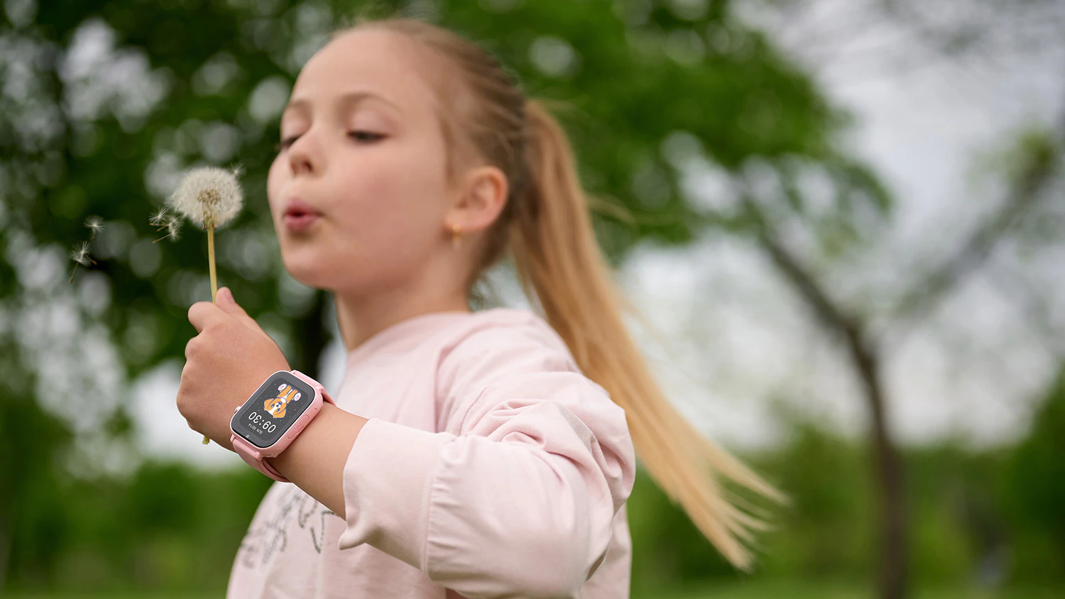 Holčička s chytrými hodinkami garett na ruce fouká do pampelišky