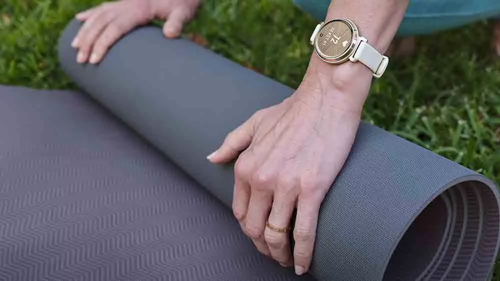 Ženské ruce s hodinkami Garmin Lily 2 balí podložku na jógu