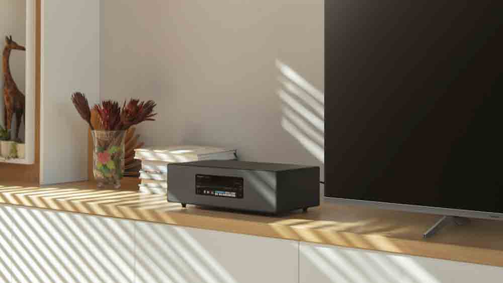 Mikrosyst&eacute;m Panasonic SC-DM502E-K stoj&iacute;c&iacute; na skř&iacute;ňk&aacute;ch vedle televize v ob&yacute;vac&iacute;m pokoji_03