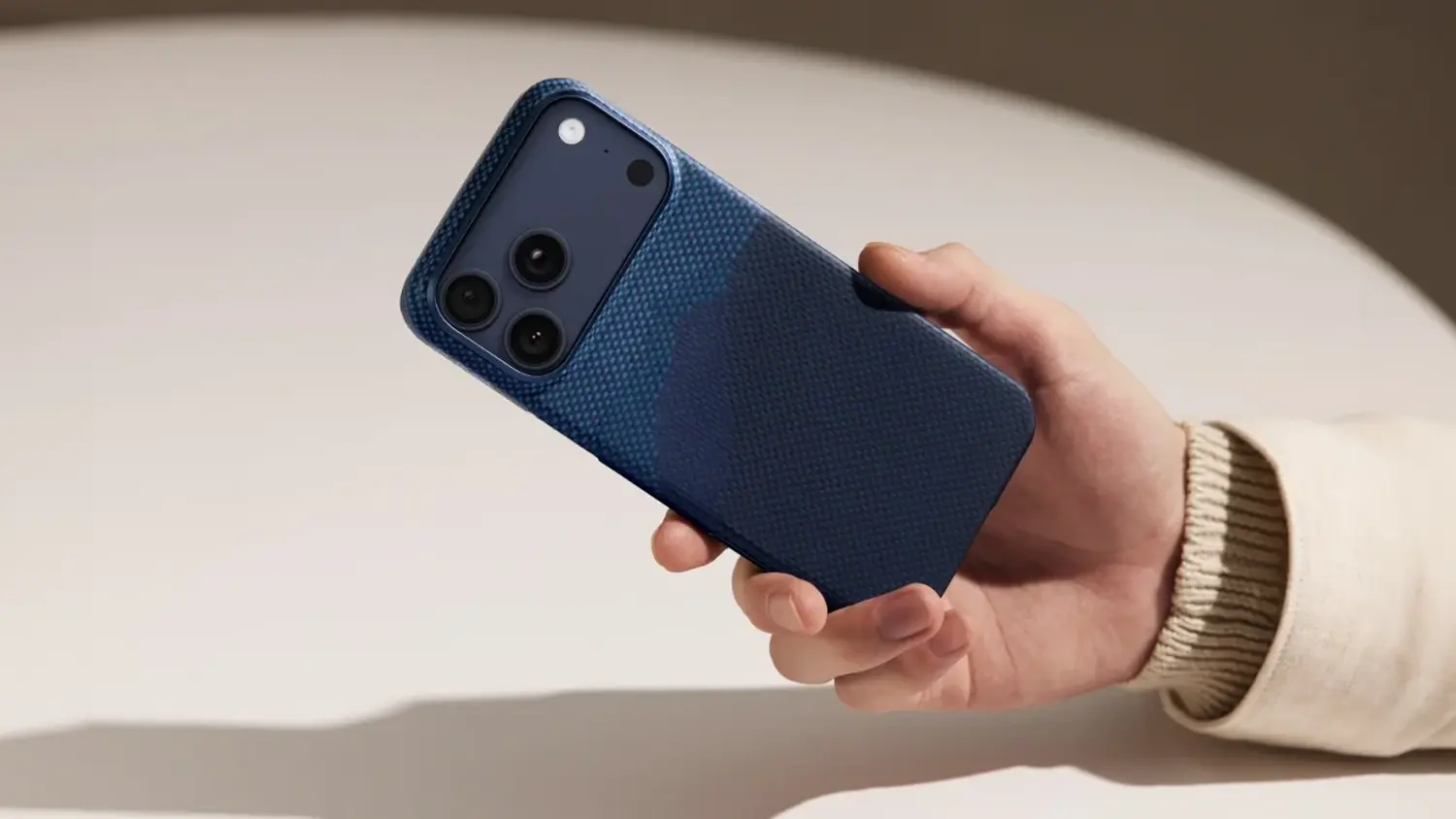 Ruka drž&iacute;c&iacute; iPhone s krytem Pitaka Aramid ProGuard iPhone 17 Pro Moonrise