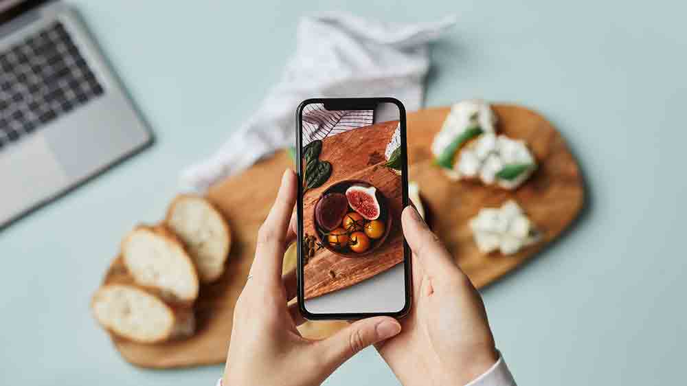 Žensk&eacute; ruce drž&iacute;c&iacute; mobiln&iacute; telefon, se kter&yacute;m fot&iacute; j&iacute;dlo na prk&eacute;nku_04