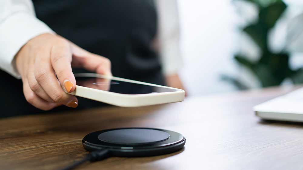 Nabíjecí podložka na stole a mužská ruka pokládající na ni mobilní telefon v silikonovém pouzdru_04