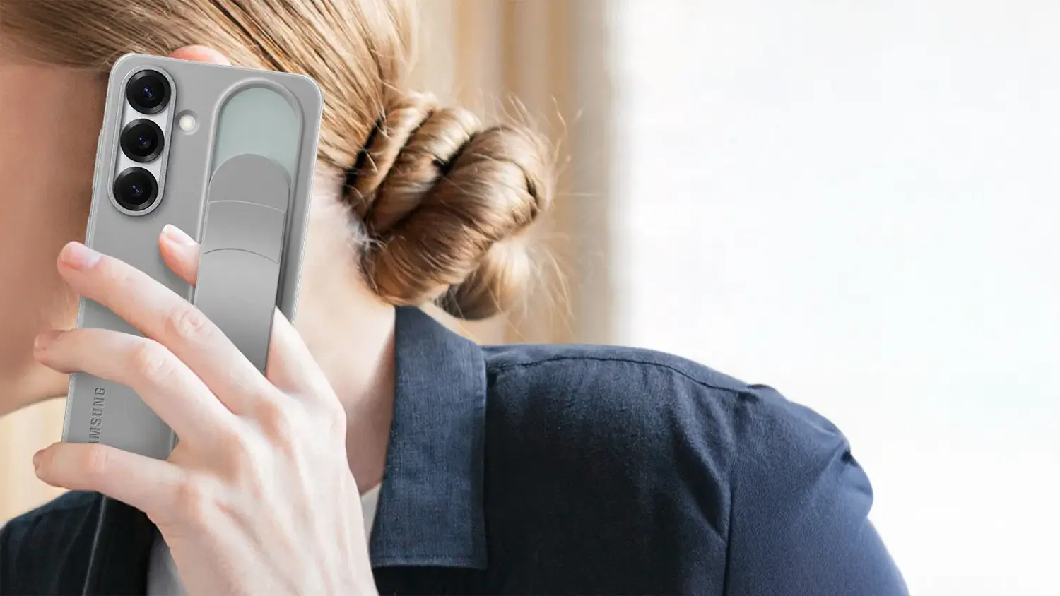 Žena drž&iacute; mobil Samsung za poutko, kter&eacute; lze použ&iacute;t i jako stoj&aacute;nek.