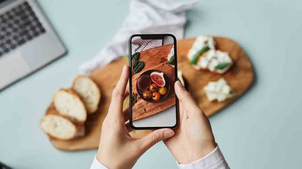 Ženské ruce držící mobilní telefon, se kterým fotí jídlo na prkénku_04