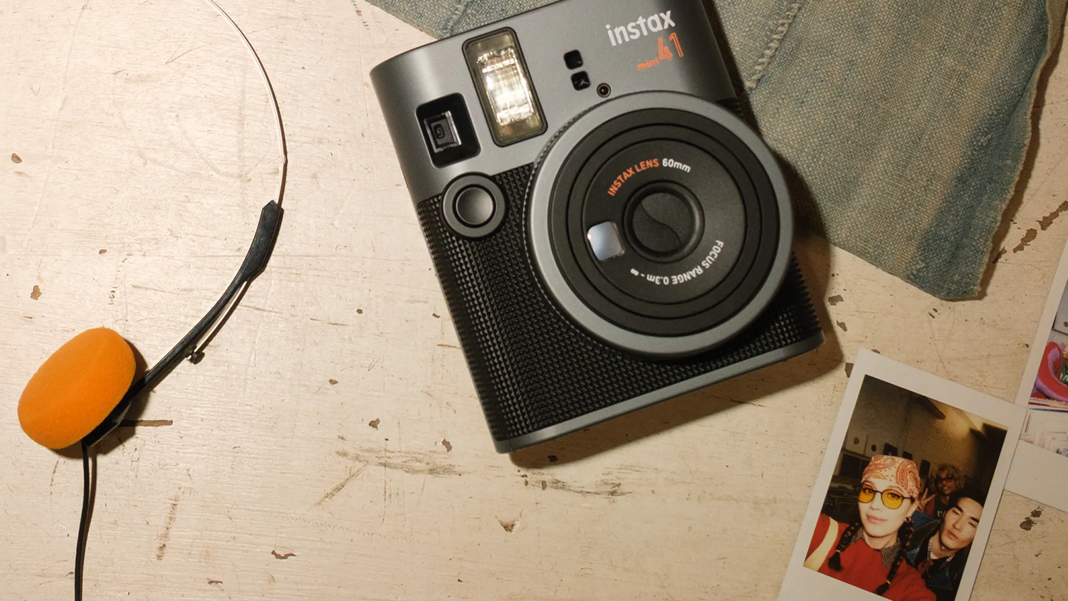 Fotoaparát Fujifilm Instax MINI 41 na stole s fotkami a sluchátky
