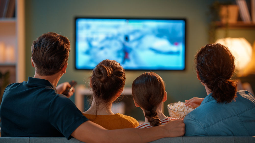 Rodina sedící na sedačce pomocí dálkového ovladače sleduje televizní program_02