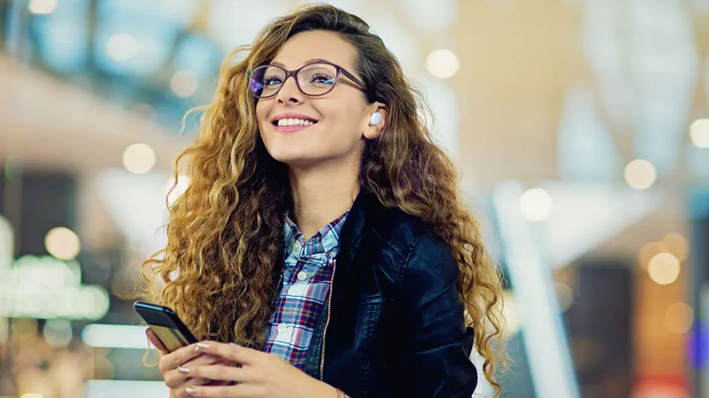 Sluchátka JVC HA-A11T v uchu dívky s mobilem v ruce_02