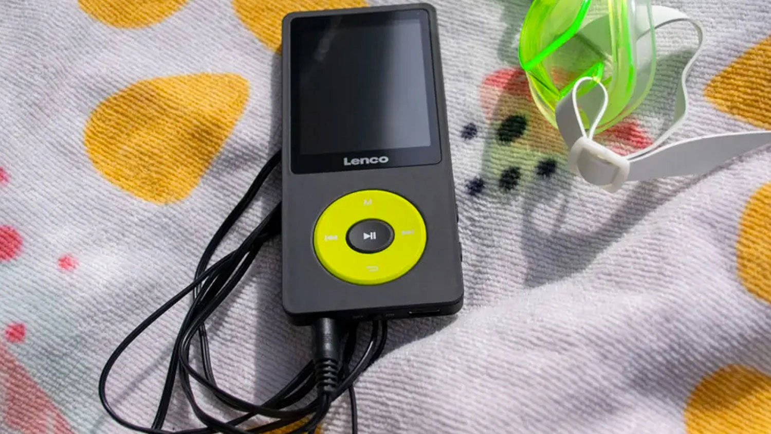 MP3/MP4 přehrávač Lenco Xemio-860 se žlutým ovládacím tlačítkem a připojenými sluchátky na osušce vedle plaveckých brýlí.