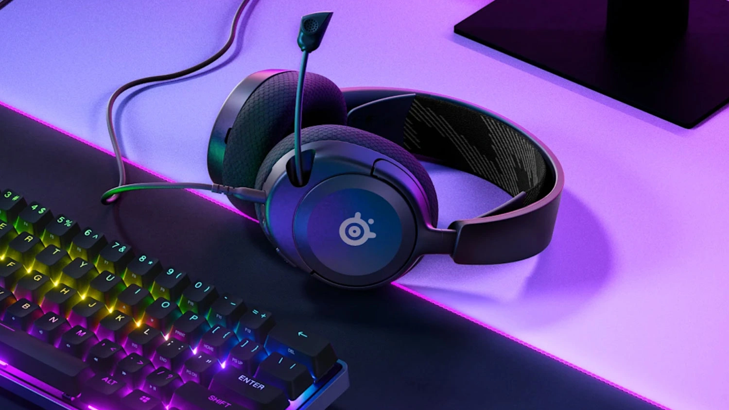 Herné slúchadlá SteelSeries Arctis Nova 1 čierne položené na stole pri klávesnici.