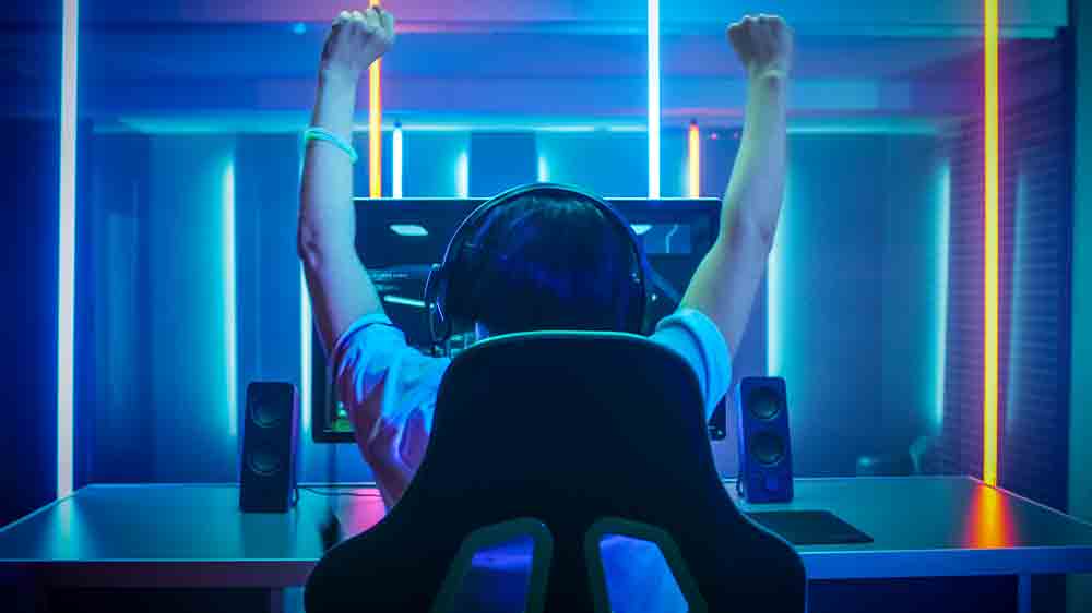 Hráč oslavující vítězství v PC hře s nasazenými sluchátky na hlavě pohledem zezadu_03