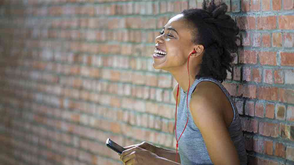 Žena opřená o zeď se sluchátky připojenými k mobilu_02