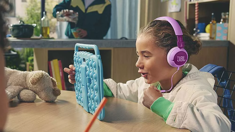 Veselá dívka hraje hru a poslouchá u toho hudbu ze sluchátek JBL JR320_02