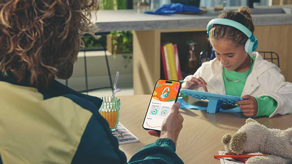Rodič sleduje na telefonu rodičovskou kontrolu, zatímco jeho dítě používá sluchátka JBL JR470NC _04
