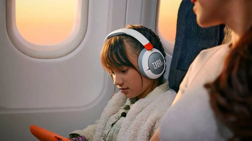 Dívka během cestování používá tablet a dětská bezdrátová sluchátka JBL Junior JR470NC_04