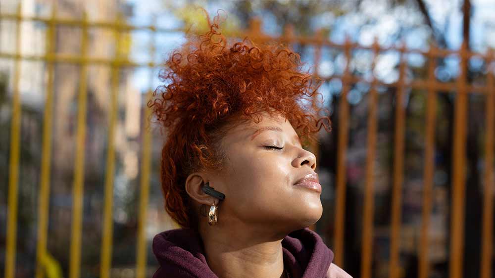 Žena s bezdrôtovými slúchadlami JBL Wave Flex 2 natáča tvár k slnku_04