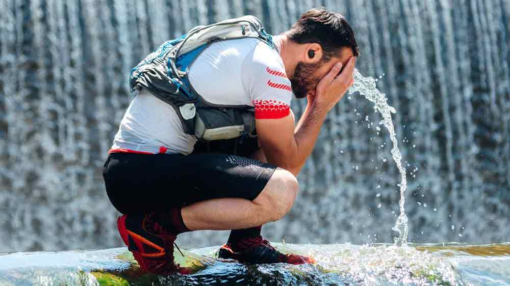 Muž s bezdrátovými sluchátky JBL Endurance Race 2 si omývá obličej u vodopádu_04