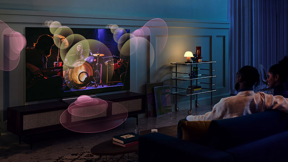 Mladý pár na pohovce sledující OLED Televizi LG OLED65A23LA, s ilustrací šíření zvuku v prostoru