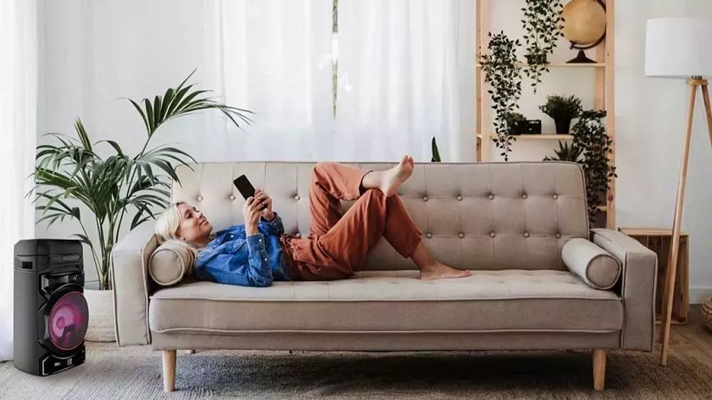 Žena lež&iacute; na pohovce a poslouch&aacute; hudbu z Bluetooth reproduktoru LG XBOOM RNC7_03