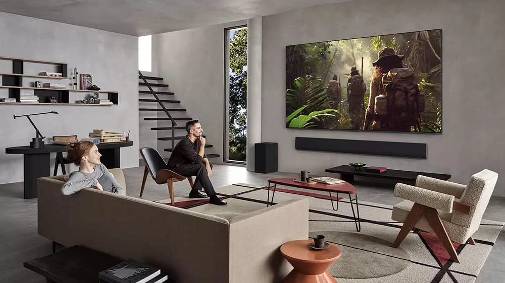 Muž a žena sleduj&iacute; v ob&yacute;vac&iacute;m pokoji OLED smart televizi LG OLED83G54LW přidělanou na stěně_03