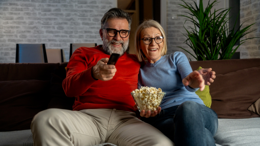 Seniorský pár na pohovce, muž míří ovladačem_02