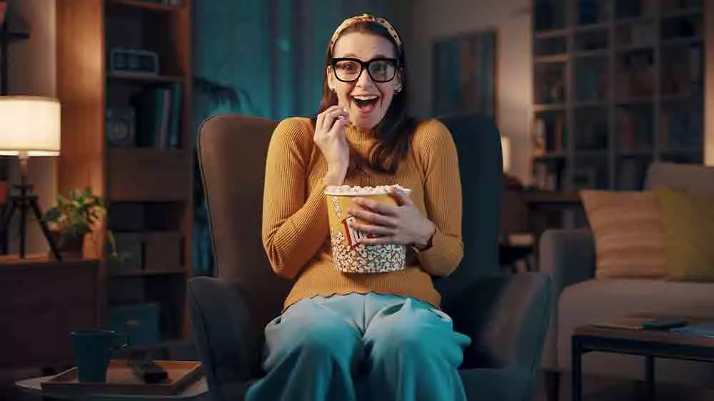 Žena sed&iacute; s popkornem v křesle a sleduje televizi_06