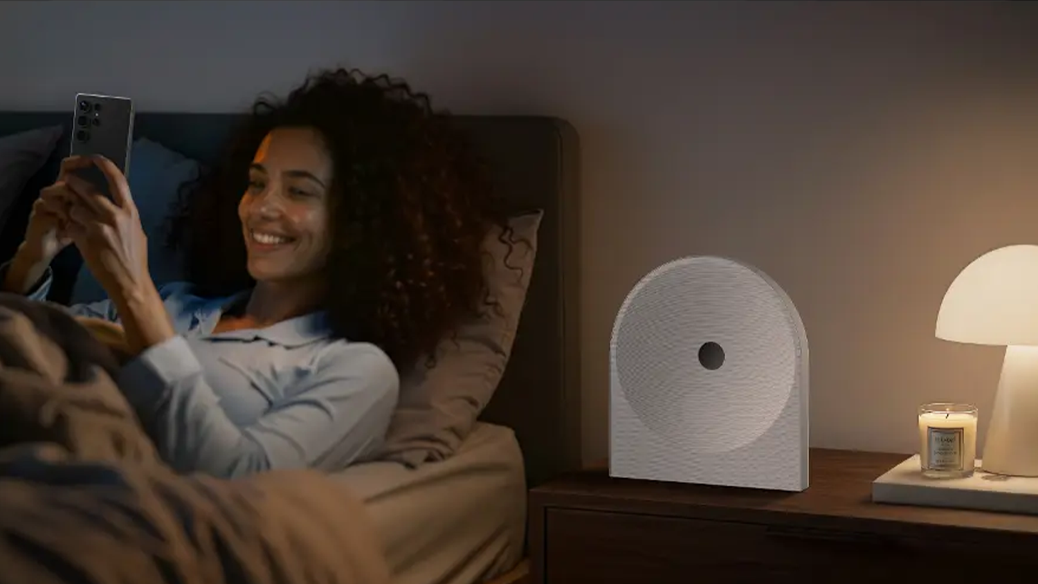 Žena si čte na mobilu, vedle ní je reproduktor Samsung