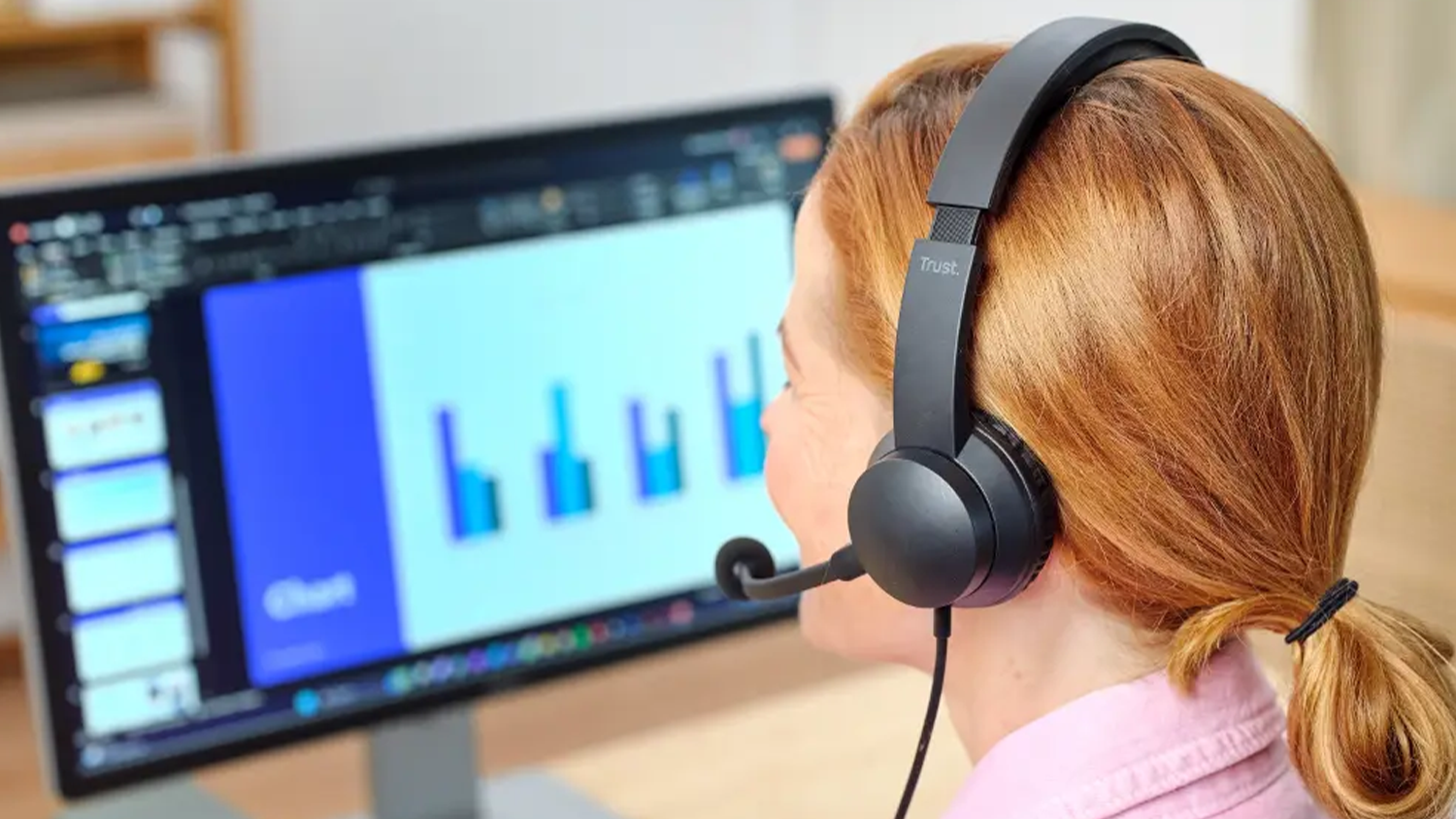 Žena pozer&aacute; na monitor s nasaden&yacute;mi sl&uacute;chadlami Trust