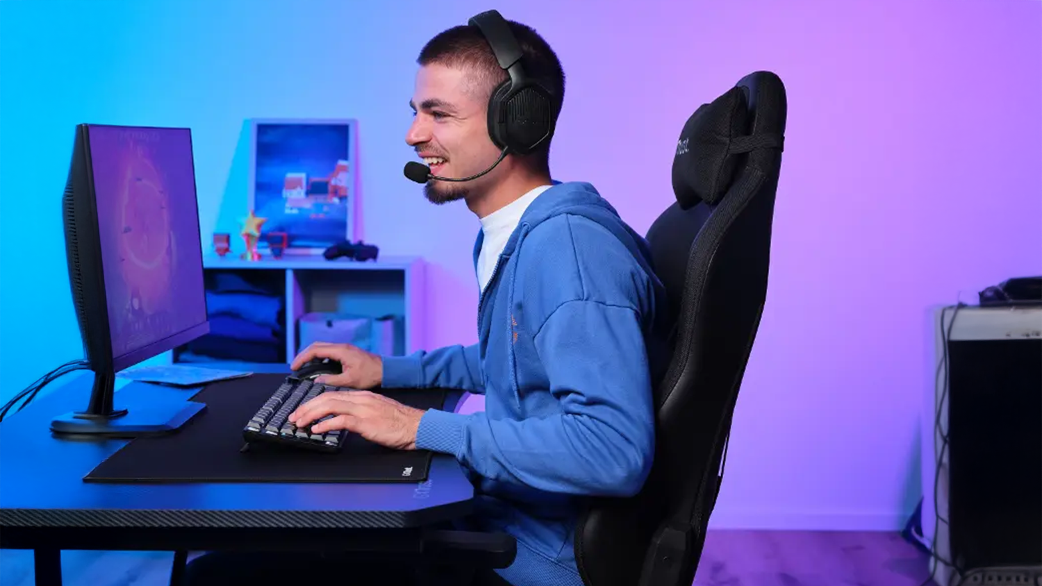 Muž sed&iacute; pri PC a hr&aacute; so sl&uacute;chadlami Trust GXT 493 Carus Black