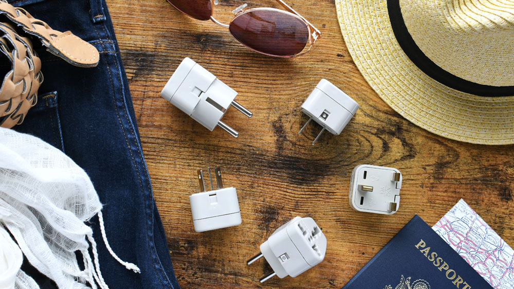 Cestovní adaptér vedle cestovatelských věcí jako pas, sluneční brýle a klobouk_02
