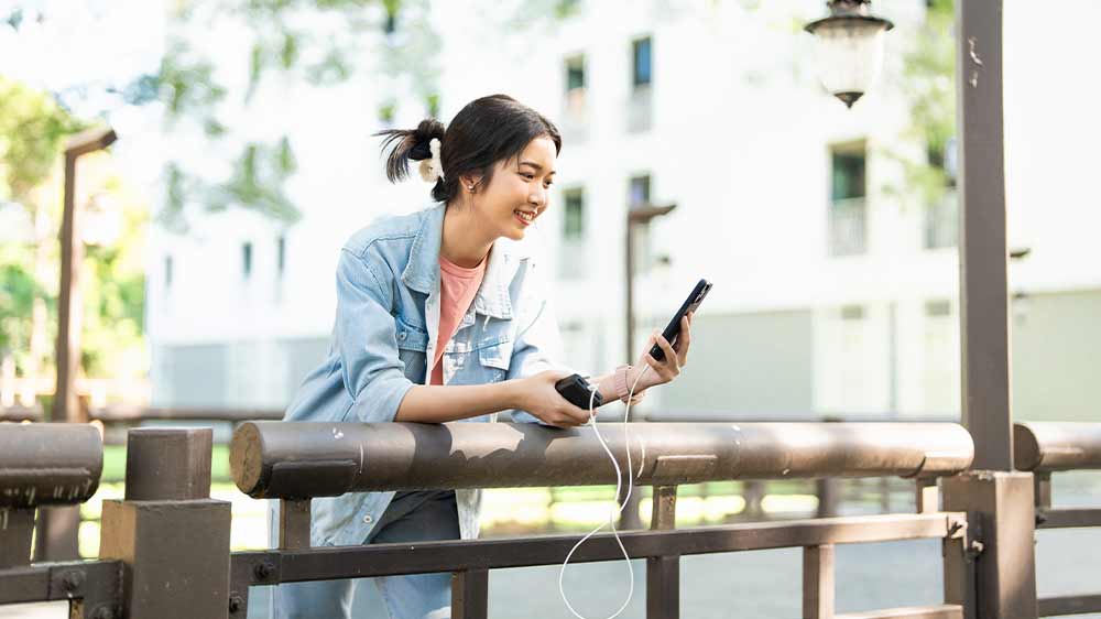Žena opřená o zábradlí nabíjí telefon přes powerbanku_03