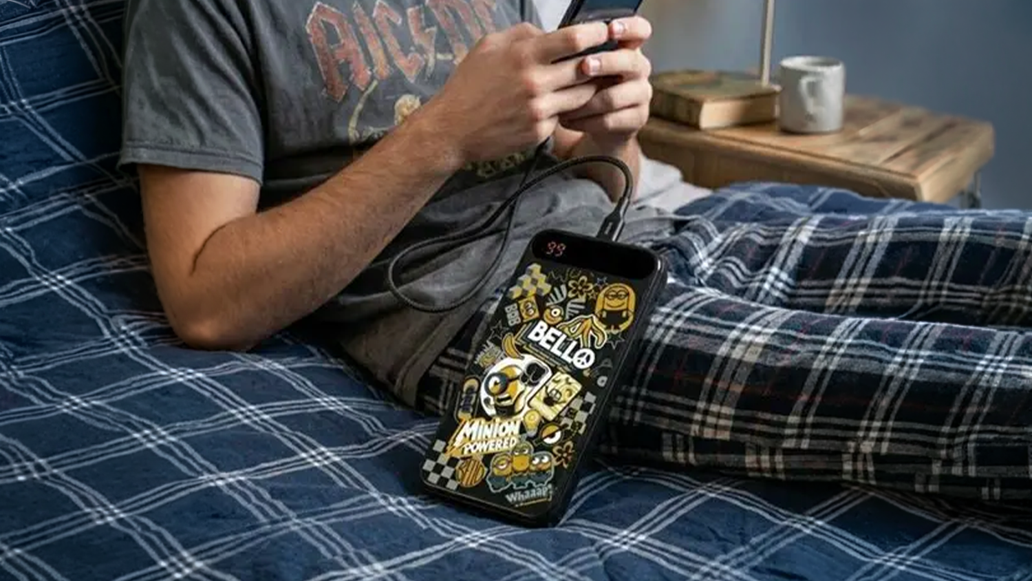 Muž lež&iacute; v posteli s telef&oacute;nom pripojen&yacute;m k powerbanke Lazerbuilt PBMN-10LI-MINIONS