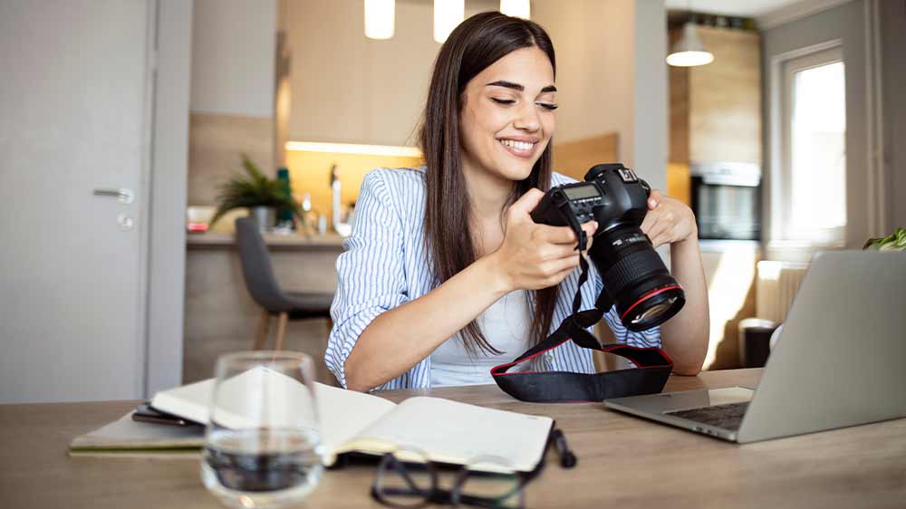 Usmívající se žena sedí u notebooku a prohlíží fotografie v digitální zrcadlovce_02