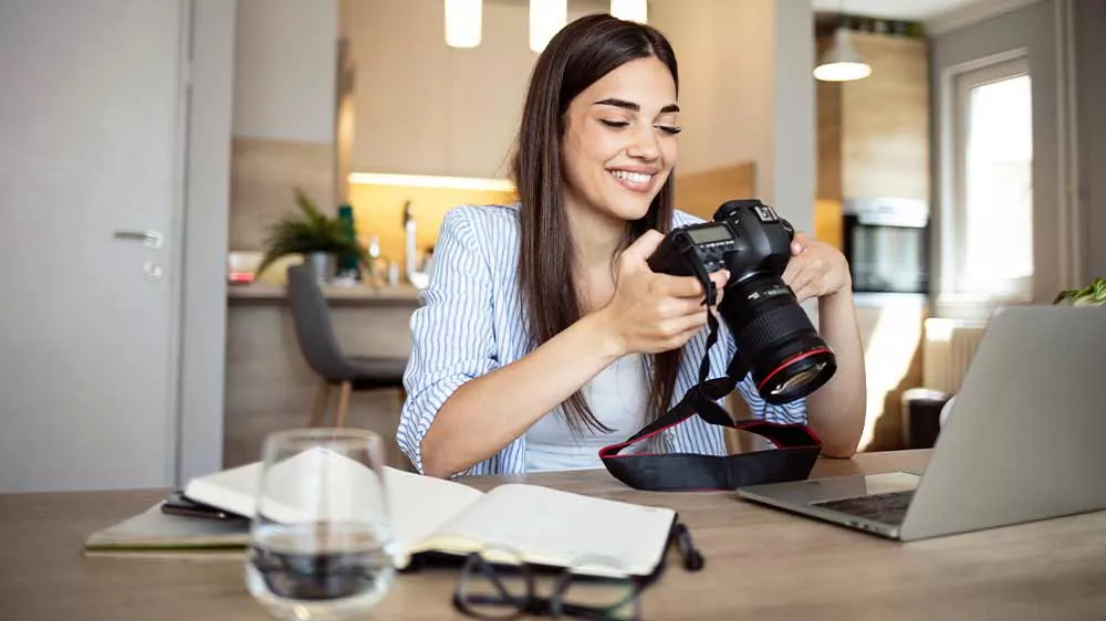 Usmívající se žena sedí u notebooku a prohlíží fotografie v digitální zrcadlovce_02