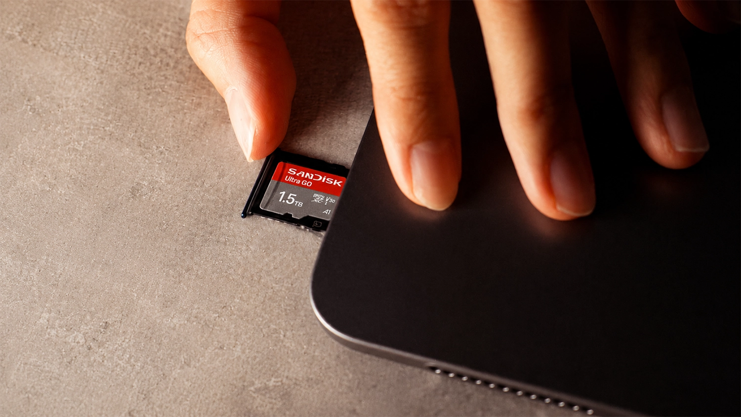 Ruka vkladá pamäťovú kartu SanDisk Ultra GO microSDXC 128 GB do slotu telefónu