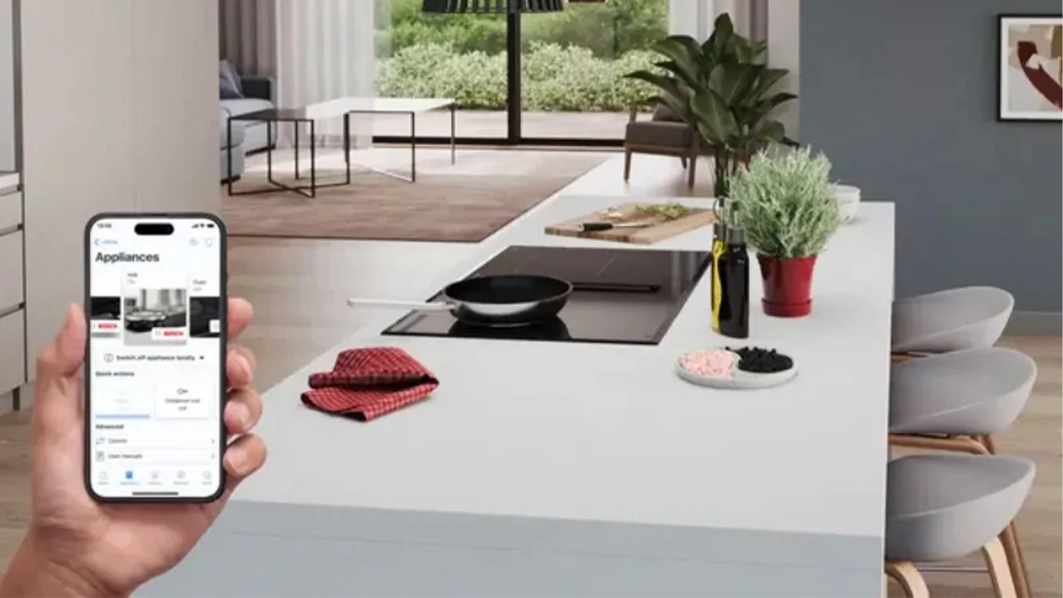 Ruka drž&iacute;c&iacute; telefon s aplikac&iacute; Home Connect kontroluj&iacute;c&iacute; varnou desku Bosch, na kter&eacute; je položen&aacute; p&aacute;nev