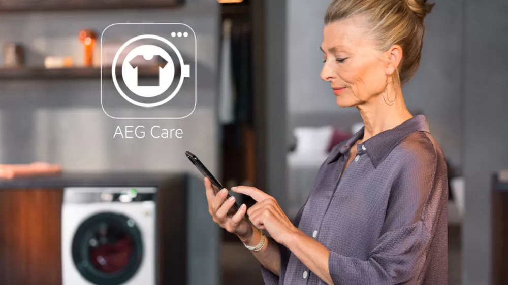 Žena drž&iacute;c&iacute; telefon s aplikac&iacute; My AEG Care na d&aacute;lku ovl&aacute;daj&iacute;c&iacute; su&scaron;ičku AEG TR959M7SC_05