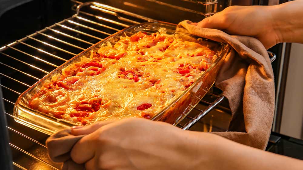 Žena vyndává upečené lasagne z trouby _04