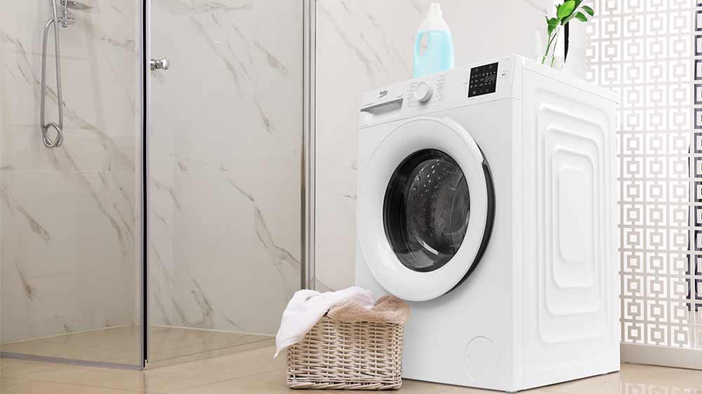 Pohled na pračku s předním plněním Beko BM1WFSU36233WW z boční strany, vedle ní stojí koš s prádlem_03