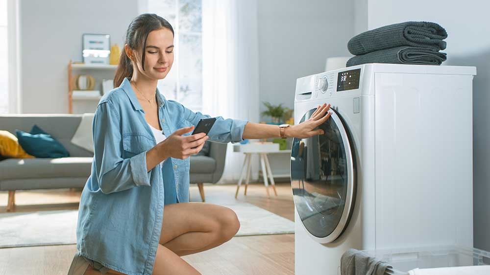Žena nastavuje pračku přes aplikaci v mobilním telefonu_04