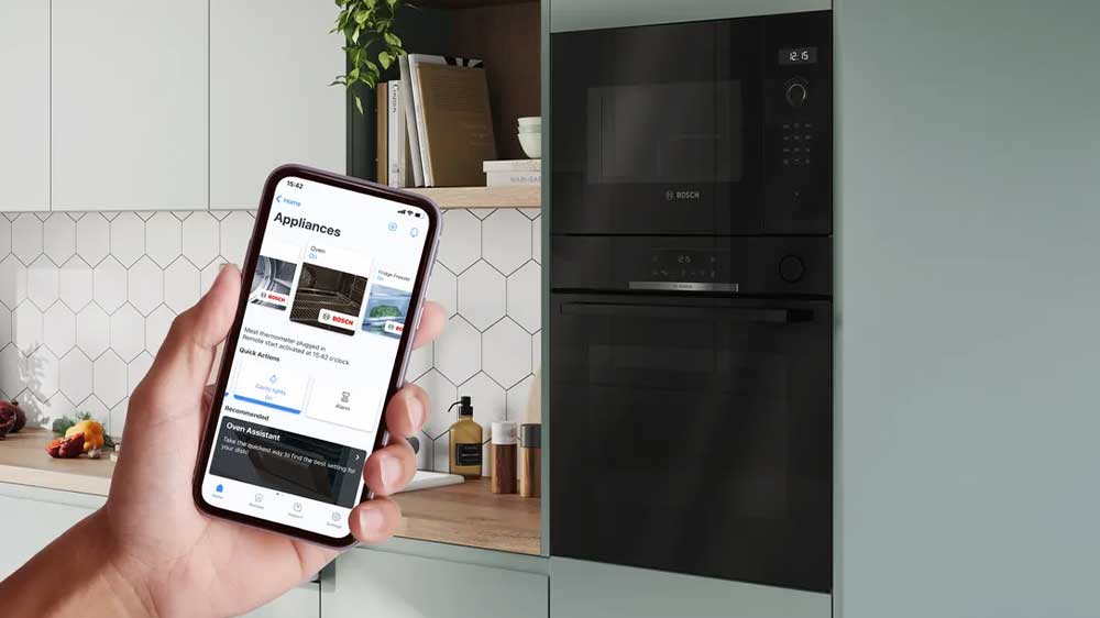 Ruka držící mobilní telefon se zapnutou aplikací k ovládání pomocí Home Connect a v pozadí kuchyňská linka se spotřebiči Bosch_04