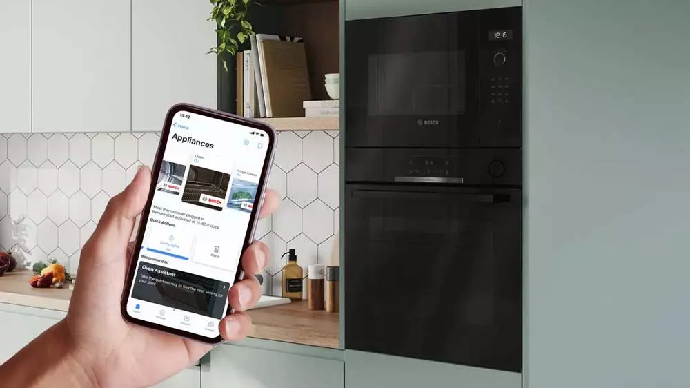 Ruka držící mobilní telefon se zapnutou aplikací k ovládání pomocí Home Connect a v pozadí kuchyňská linka se spotřebiči Bosch_04